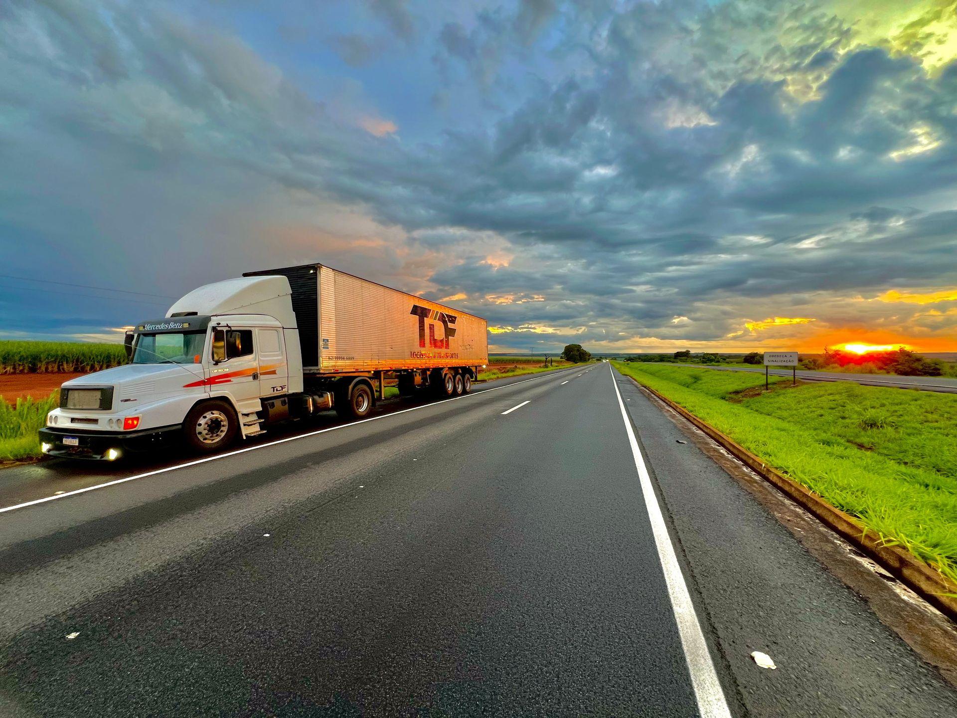 Semi truck parked beside a highway at sunset with dramatic clouds in the sky.